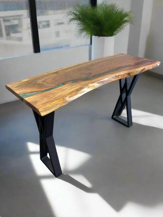 A walnut console table with a gunship green epoxy river through the length of it, paired with black "X" shaped legs, sitting in a white modern office with plants and a large window.