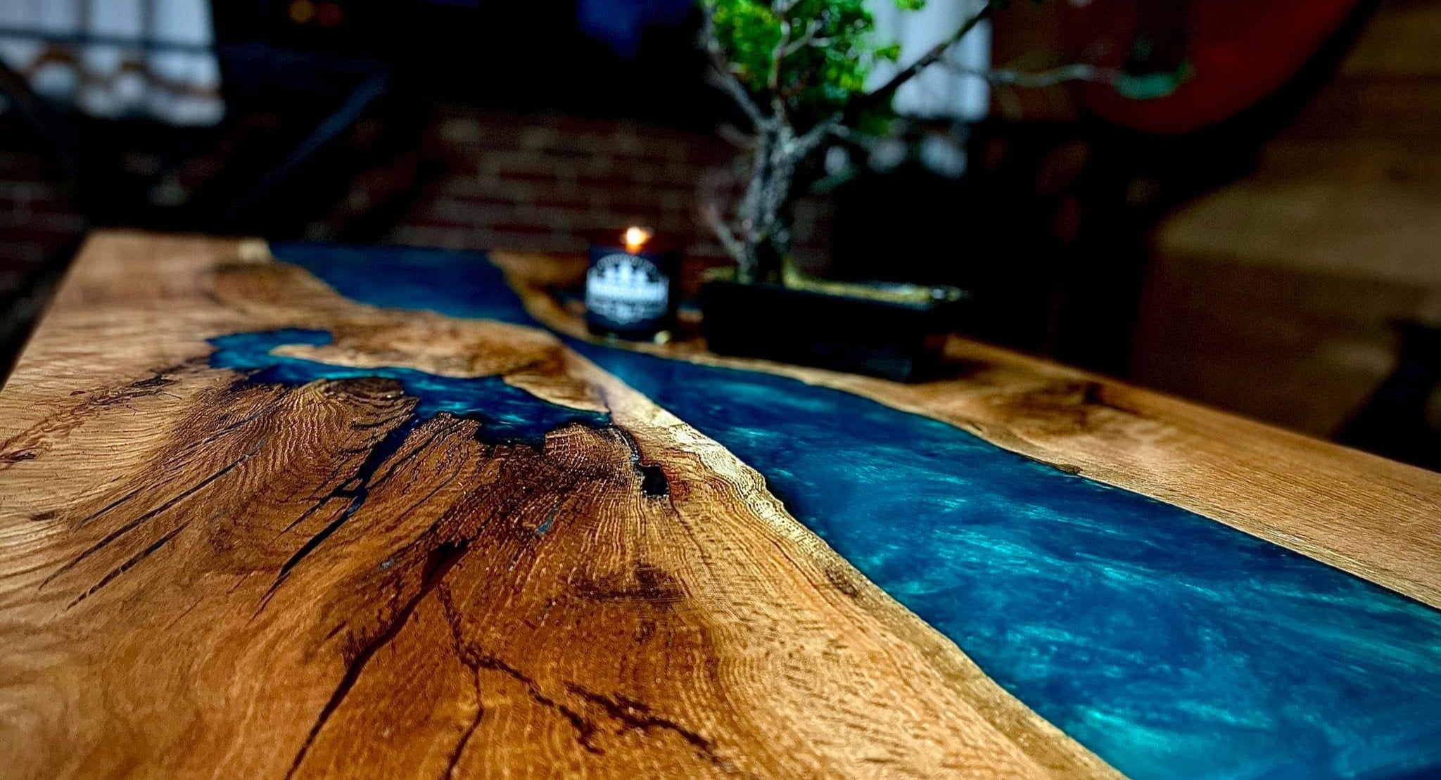 A close up of an organic, light brown table featuring a river of sky blue epoxy, as well as a  black mug in the background. 